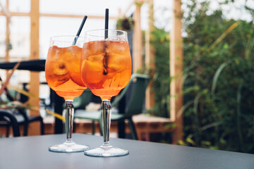 Two glasses of Aperol Spritz served on the terrace of modern bar. Popular Italian wine based cocktail and summer aperitif refreshing drink prepared with prosecco wine, bitter liqueur and soda water.