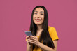© Prostock-studio - Cool gadget and app. Happy korean lady using smartphone and smiling at camera, standing on violet studio background