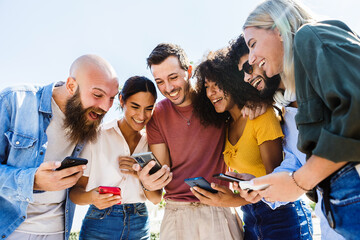 young group of happy people smiling while using mobile phone together - smiling multiracial friends 
