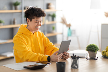 Wall Mural - Smiling asian man using digital tablet at home