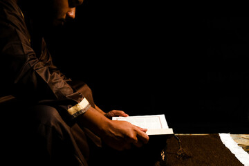 Selective focus picture of a men reading Holy Quran on copyspace dark background. Always Quran concept.