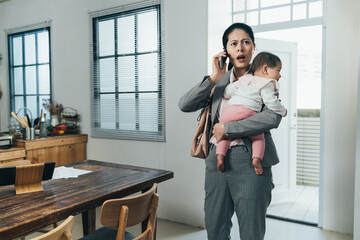 Wall Mural - asian female ceo carrying toddler just getting home is receiving emergent phone call from company. chinese businesswoman with baby opening mouth wide is surprised at a bad news she hears on phone.