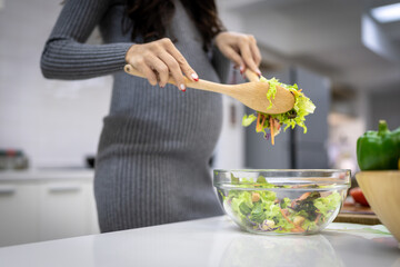 Healthy and cheerful pregnant woman preparing food for herself in her home kitchen. The menu is a vegetable and fruit salad.