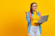 © Bangun Stock Photo - Portrait of smiling young Asian woman student in casual wear with backpack using laptop and pointing at copy space with finger isolated on yellow background. Education in college university concept