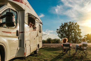 Children leaning out of the window of the caravan, watching their mothers drinking coffee. Concept of family in caravan