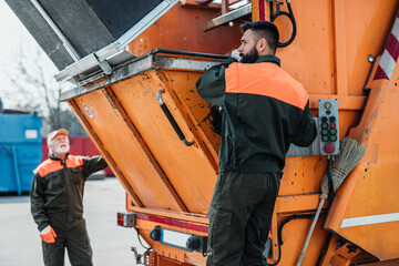 Sticker - Senior and young garbage men working together on emptying dustbins for trash removal.