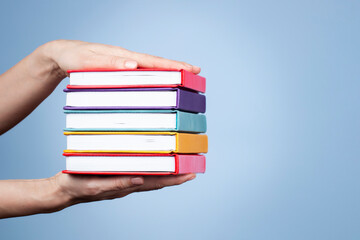 Wall Mural - Female hands holding pile of books over light blue background. Education, self-learning, book swap, hobby, relax time