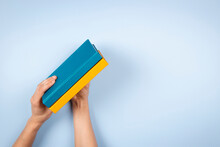 Female Hands Holding Two Blue And Yellow Color Books Over Light Blue Background. Education, Self-learning, Book Swap