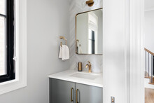 Contemporary White And Gray Half Bathroom. Gray Bathroom Vanity With Gold Fixtures And Mirror Showing Into Hallway.