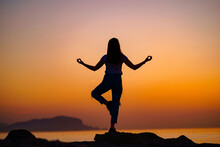 Back View Of Free Calm Bliss Satisfied Woman Standing On Top Rock With Yoga Position Against Of Idyllic Sunset Sky By The Sea In A Happy Beautiful Inspired Moment Of Her Life