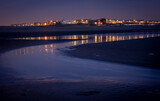 Fototapeta Łazienka - Wieczór nad morzem, plaża, woda wpływająca.  W dali światła miasteczka nadmorskiego.