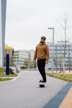 Young Man In A Helmet Rides An Electric Skateboard. Onewheel Rider In An Urban Background. Copy Space Vertical