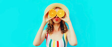 Summer Portrait Of Cheerful Young Woman Covering Her Eyes With Slices Of Orange Fruits And Looking For Something Wearing Straw Hat On Blue Background