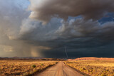 Fototapeta  - Dirt road with dark, ominous storm clouds and lightning