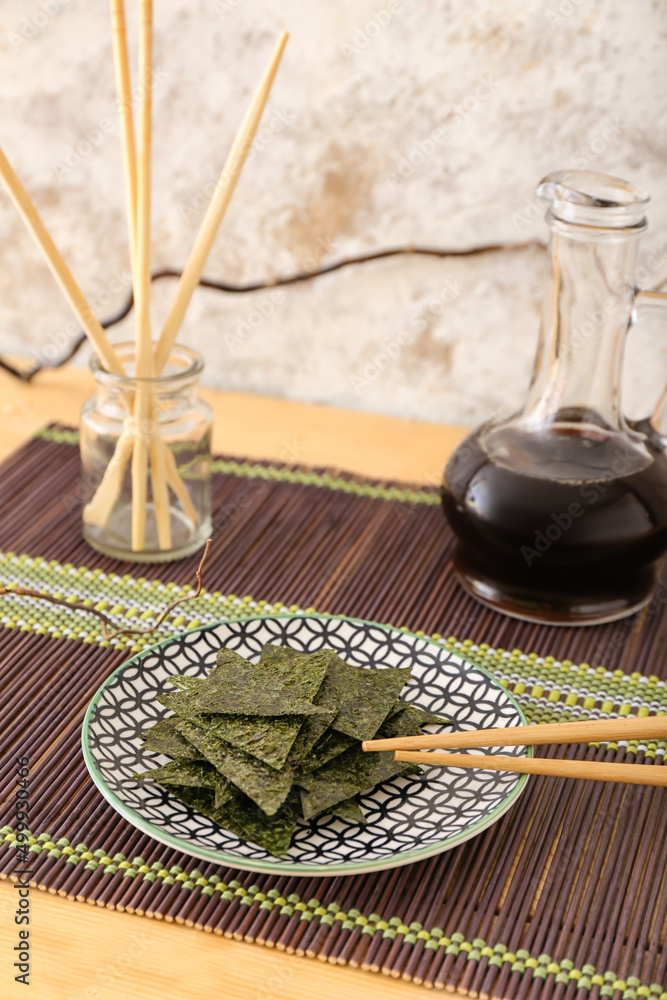 Plate of tasty seaweed sheets on table near light wall