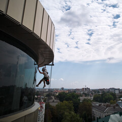 Wall Mural - Industrial mountaineering worker cleaning glass window of skyscraper. Male cleaner using safety lifting equipment while washing window of high-rise building.