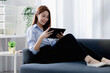 © kamiphotos - A woman plays a tablet on the sofa in her living room at home, she is resting on weekends after a hard day's work, she relaxes by watching movies and listening to music on her tablet. Holiday concept.