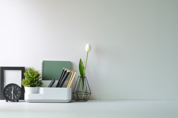 Wall Mural - Feminine workplace with picture frame, stationery and flower pot on white table. Copy space.