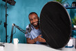 Portrait of photography equipment reviewer presenting beauty dish honeycomb grid in vlogging studio. Vlogger explaining features of studio flash light modifier sitting at desk with microphone.