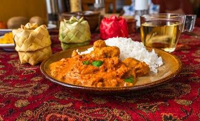Chicken tikka masala with rice on plate, 3 bamboo spice box, cup of tea on red table-cloth on table.