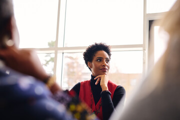 Portrait of pensive mature black businesswoman listening with hand on chin in meeting room