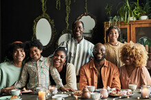 Portrait Of Big African Family Smiling At Camera While Sitting At Table With Dessert In Dining Room