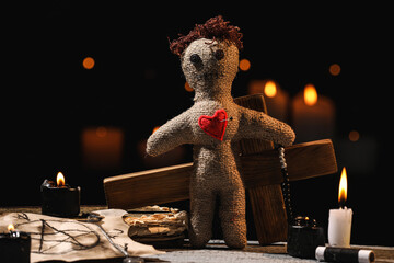 Wall Mural - Voodoo doll with pin in heart and ceremonial items on wooden table against blurred background