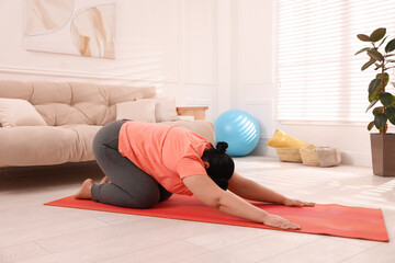 Sticker - Overweight mature woman doing exercise on yoga mat at home