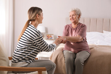 Wall Mural - Young caregiver talking to senior woman in bedroom. Home care service