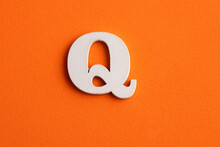 Alphabet Letter Q - White Wood Piece On Orange Foamy Background