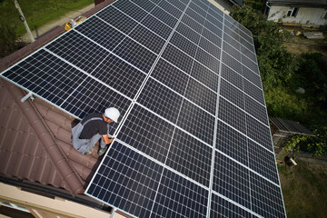 Man worker mounting photovoltaic solar moduls on roof of house. Engineer in helmet installing solar panel system outdoors. Concept of alternative and renewable energy. Aerial view.