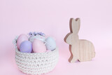 Fototapeta  - Ozdoby wielkanocne, drewniany zając, kosz z pastelowymi jajkami, pisankami, na jasno różowym tle