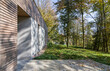 Fragment elewacji domu jednorodzinnego wśród drzew wykonany z drewna i betonu.