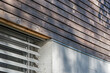 Detal architektoniczny na fragment elewacji domu jednorodzinnego wykonanego z drewna i betonu. Widoczne okno z żaluzjami aluminiowymi elewacyjnymi