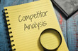 Closeup shot of a yellow notebook page with a magnifying glass and the writing competitor analysis