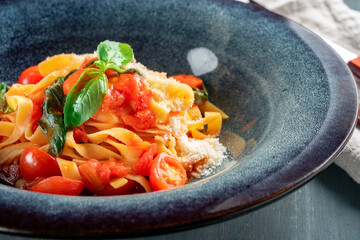 Wall Mural - The classic tagliatelli pasta with tomato sauce is served on a blue plate. Italian dish with tomatoes, basil, parmesan and pasta, closeup