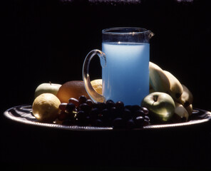 Wall Mural - Still life with a glass jug of blue lemonade and fruits on a tray isolated on a black background