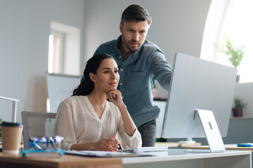 Young female trainee working on computer together with her business mentor at modern company office