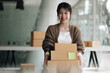 © wichayada - Happy young asian woman startup small business freelance holding parcel box and computer laptop. Online marketing packing box delivery concept