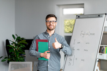 Sticker - Positive mature male teacher showing thumb up standing near blackboard, recommending new online foreign languages school