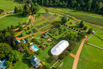 Canvas Print - Aerial view of rural ranch with planted field near to a dense forest in bright sunlight