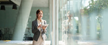 Attractive Business Asian Woman Standing Near Window And Using Smart Digital Tablet.