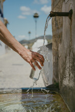 Vertical Photo Of A Hand Holding A Glass Bottle While Water Overflows From The Bottle. Water Falls From A Natural Spring Water Source.
