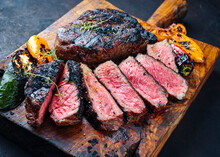 Traditional Barbecue Dry Aged Wagyu Rib-eye Beef Steaks Served With Paprika And Zucchini As Close-up On An Old Rustic Wooden Board