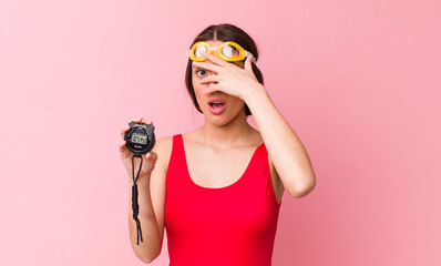 Poster - hispanic pretty woman looking shocked, scared or terrified, covering face with hand. swimmer and timer concept