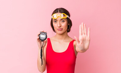 Poster - hispanic pretty woman looking serious showing open palm making stop gesture. swimmer and timer concept