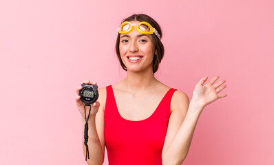 Poster - hispanic pretty woman smiling happily, waving hand, welcoming and greeting you. swimmer and timer concept