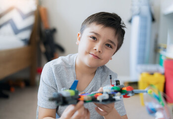 Portrait kid playing plastic blocks, Happy Child relaxing sitting on carpet building his colourful blocks toys in bedroom, Young boy with smiling face looking at camera while holding toy.