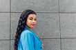 © Dani D.G - Woman in her 20s wearing blue trend clothes, looking at the camera. Modern African young adult woman walking through the city streets with a wall in the background.