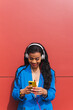 © Dani D.G - African young woman using smart phone on red background and blue clothes.